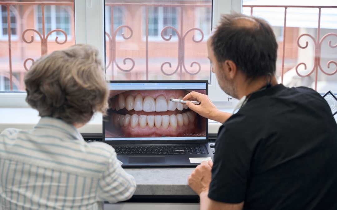 Dentist consulting with patient while reviewing digital smile design on laptop screen.