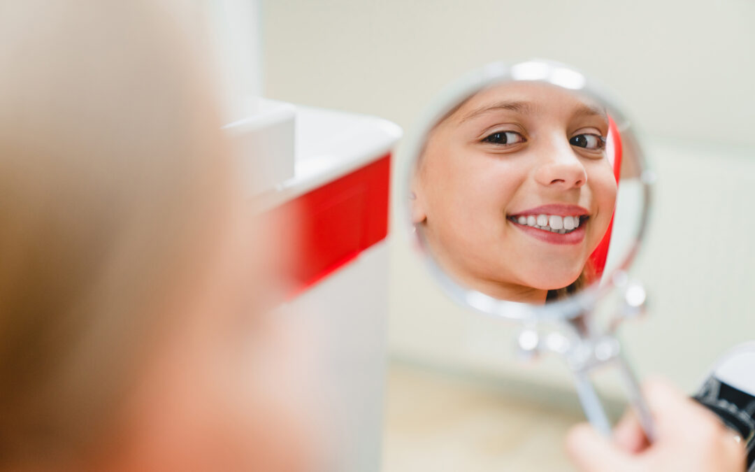 Child smiling while looking in handheld mirror during dental visit in Scottsdale.