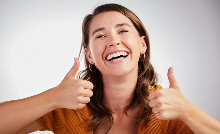 Woman giving thumbs up while smiling, representing positive dental care results.